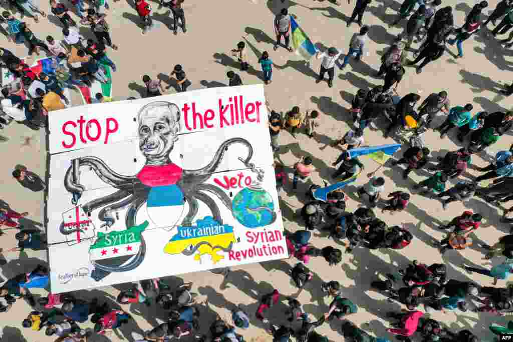 Protesters raise a giant sign depicting Russia&#39;s President Vladimir Putin as an octopus with its arms wrapping around the countries of Georgia, Syria and Ukraine, as well as the world globe, during a demonstration in the city of Binnish in Syria&#39;s northwestern rebel-held Idlib province.