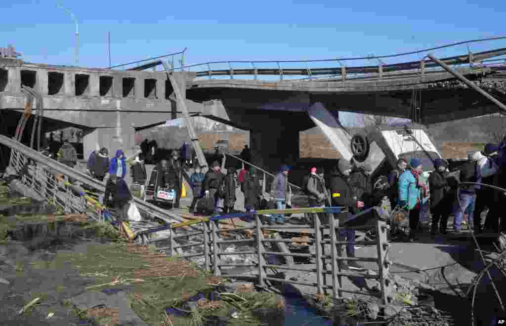 Ucranianos cruzan un camino improvisado debajo de un puente destruido mientras huyen de Irpin, a unos 25 km (16 millas) al noroeste de Kiev, el viernes 11 de marzo de 2022.&nbsp;(Foto AP/Efrem Lukatsky)