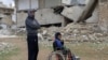 FILE - Mahmoud Madarati, 55, poses as he stands near his son whose leg and hand were amputated after sustaining injuries by what Mahmoud says was shelling from government-held areas, northern Syria, March 3, 2022. 