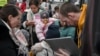 A woman holds a child as a humanitarian aid worker checks the identities of refugees boarding a bus bound for Portugal outside the main shelter and relocation center in Przemysl, southeastern Poland on March 16, 2022.