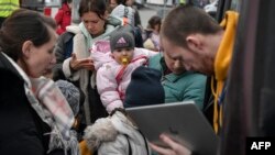 A woman holds a child as a humanitarian aid worker checks the identities of refugees boarding a bus bound for Portugal outside the main shelter and relocation center in Przemysl, southeastern Poland on March 16, 2022.