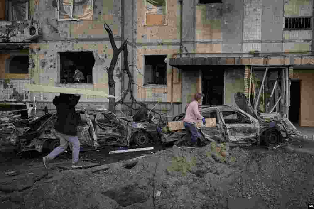 La gente lleva tablas de madera para cubrir las ventanas de un edificio dañado por un bombardeo el día anterior en Kiev, Ucrania, el lunes 21 de marzo de 2022.&nbsp; (AP Photo/Vadim Ghirda).