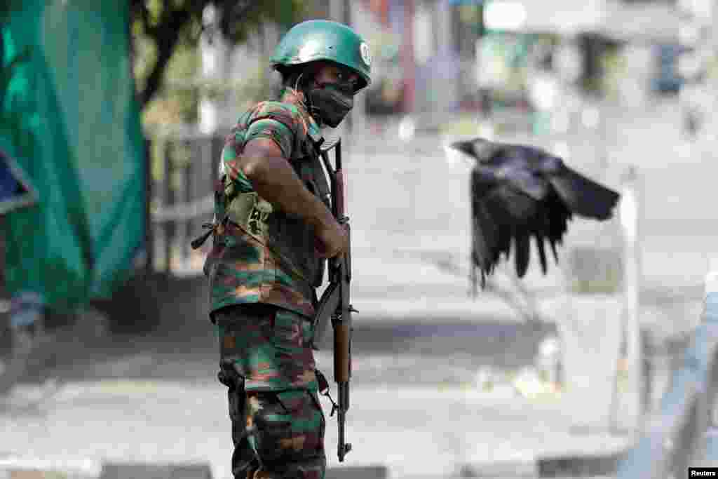 A crow flies by as a Sri Lankan army soldier stands guard on a main road after the government imposed a curfew following a clash between police and protesters near Sri Lankan President Gotabaya Rajapaksa&#39;s house, April 3, 2022. (REUTERS/Dinuka Liyanawatte)