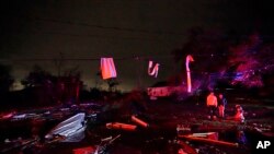 Residents illuminated by fire truck lights stand amongst debris after a tornado in Arabi, La., Tuesday, March 22, 2022. A tornado tore through parts of New Orleans and its suburbs Tuesday night, ripping down power lines and scattering debris in a part of the city that had been heavily damaged by Hurricane Katrina 17 years ago.