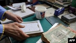 Seorang pria tampak menyusun halaman Al-Quran menjadi satu dalam pelatihan restorasi Al-Quran lama di Tripoli, Libya, pada 22 Maret 2022. (Foto: AFP/Mahmud Turkia)