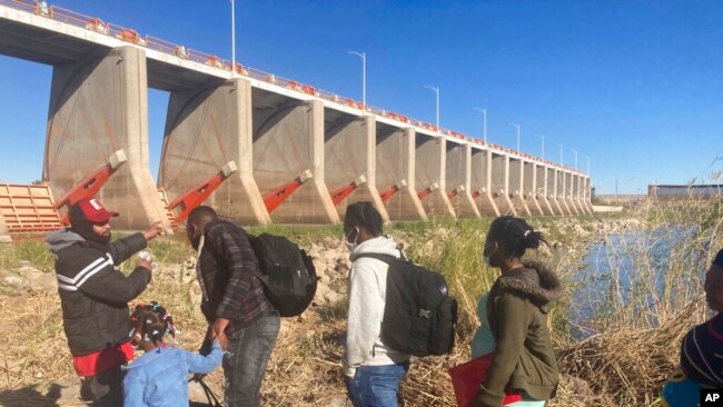 FILE - A Mexican smuggler guides a Haitian family across the Morelos Dam over the Colorado River from Los Algodones, Mexico, on Feb. 4, 2022, to Yuma, Ariz.