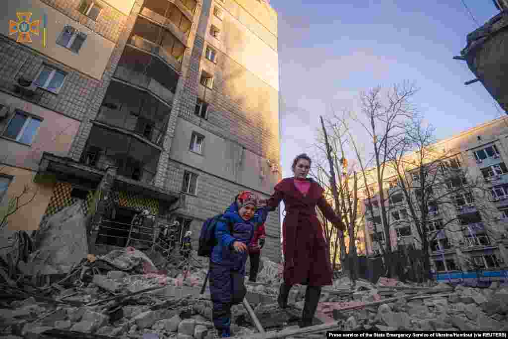 A woman with a child evacuates from a residential building damaged by shelling in Kyiv in this handout picture released March 16, 2022.