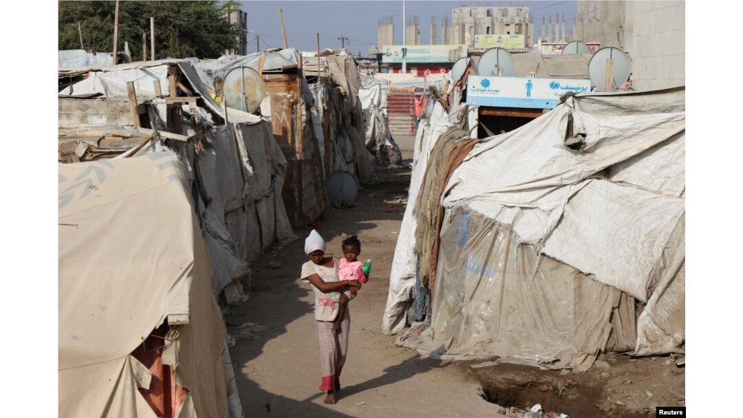 Seorang anak perempuan menggendong anak kecil melalui kemah-kemah sementara untuk para pengungsi (IDP) di Aden, Yaman, 15 Maret 2022. (REUTERS/Fawaz Salman)