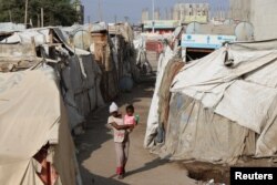 Seorang anak perempuan menggendong anak kecil melalui kemah-kemah sementara untuk para pengungsi (IDP) di Aden, Yaman, 15 Maret 2022. (REUTERS/Fawaz Salman)