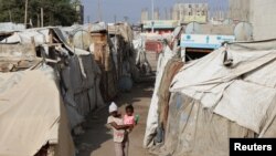 Seorang remaja perempuan tampak menggendong seorang anak kecil ketika ia berjalan di kawasan tenda pengungsi sementara di Aden, Yemen, pada 15 Maret 2022. (Foto: Reuters/Fawaz Salman)