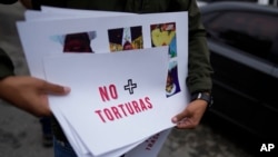 A protester holds a sign that says in Spanish "No more torture" during a protest against politics outside the Bolivarian prisoners National Intelligence Service (SEBIN), known as the Helicoide, in Caracas, Venezuela, Wednesday, Nov. 3, 2021.
