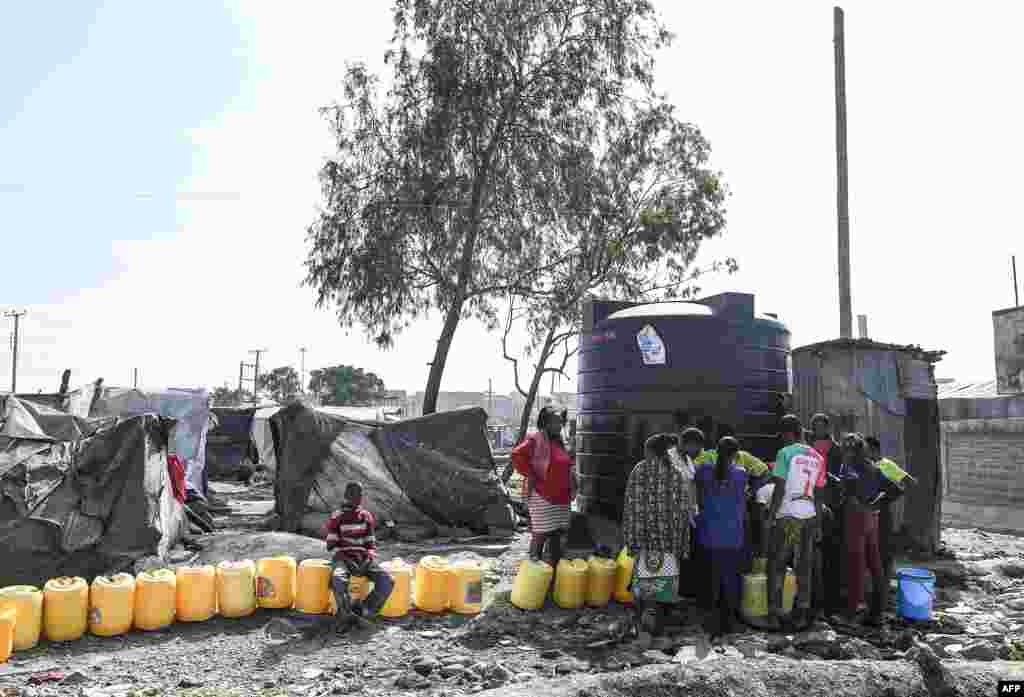 Women with containers get in line for water next to their temporary camp, in the Mukuru Kwa Njenga informal settlements, Kenya. (Photo by Simon MAINA / AFP)