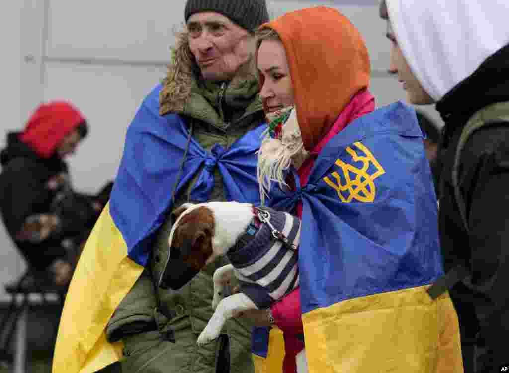 A woman and a man, wrapped in Ukrainian flags hold a dog as they arrive at a humanitarian aid center, for displaced persons fleeing Ukraine, in Przemysl, Poland, March 8, 2022.