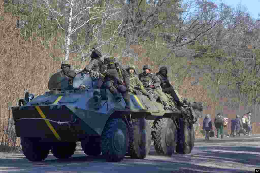 Ukrainian soldiers on an armored personnel carrier pass by people carrying their belongings as they flee the conflict, in the Vyshgorod region close to Kyiv, March 10, 2022.&nbsp;Russia&rsquo;s two-week-long war in Ukraine has killed thousands of people and forced more than 2 million others to flee the country, shaking the foundations of European security.