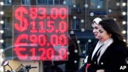 FILE - People walk past a currency exchange office screen displaying the exchange rates of U.S. dollar and euro to Russian rubles in Moscow's downtown, Russia, Feb. 28, 2022. 