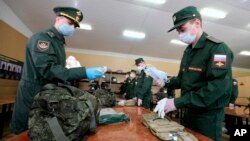 FILE - A Russian officer, left, hands face masks to a conscript at a military conscription office in Moscow, May 22, 2020. 