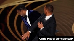 Will Smith, right, hits presenter Chris Rock on stage while presenting the award for best documentary feature at the Oscars, March 27, 2022, at the Dolby Theatre in Los Angeles.