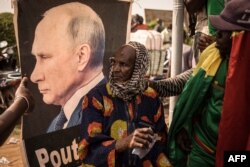 Seorang pria duduk di depan potret Presiden Rusia Vladimir Putin selama demonstrasi yang diselenggarakan oleh platform pan-Afrika Yerewolo untuk merayakan pengumuman Prancis untuk menarik pasukan Prancis dari Mali, di Bamako, 19 Februari 2022. (FLOREN VERGNES / AFP)