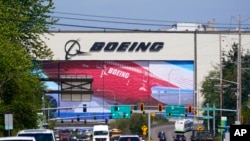 FILE - Traffic drives in view of a massive Boeing Co. production plant, where images of jets decorate the hangar doors, April 23, 2021, in Everett, Wash.