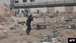 FILE: A member of SAPS shoots rubber bullets to disperse a crowd looting outside a warehouse storing alcohol in Durban on July 16, 2021, in the midst of an ongoing alcohol ban after protestors have clashed with police following a week of unrest in South Africa.