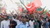 A police officer reacts as the supporters of Pakistani Prime Minister Imran Khan, chairman of the Pakistan Tehreek-e-Insaf (PTI) political party, wave flags as he lands from a helicopter to attend a public rally in Islamabad, Pakistan, March 27, 2022. 