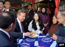 Maudy Ayunda (tengah) saat bertugas mendampingi PM Inggris David Cameron (kiri) mencicipi makanan lokal dari warung pinggir jalan di luar masjid Sunda Kelapa, Jakarta, 28 Juli 2015, sebelum berdialog dengan organisasi Islam. (Foto: Yudhi Mahatma/AFP)