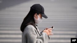 Žena koja nosi masku gleda u svoj telefon u srijedu, 16. marta 2022., u Pekingu.