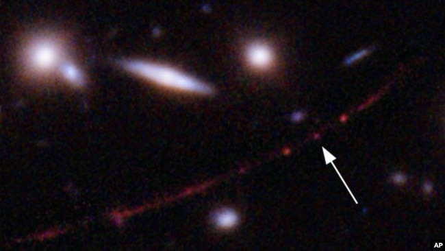 This image made available by NASA on Wednesday, March 30, 2022, shows the star Earendel, indicated by arrow, and the Sunrise Arc galaxy, stretching from lower left to upper right. 