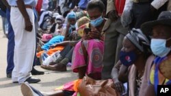 FILE: A woman reads messages on her mobile phone while waiting in a bank queue in Harare, Zimbabwe on Monday, Dec. 13, 2021. In Zimbabwe and other African nations, the virus's resurgence is threatening the very survival of millions of people