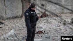 在基辅一处被俄罗斯无人机破坏的建筑附近，一名警察站在无人机残骸边。(2022年12月14日)