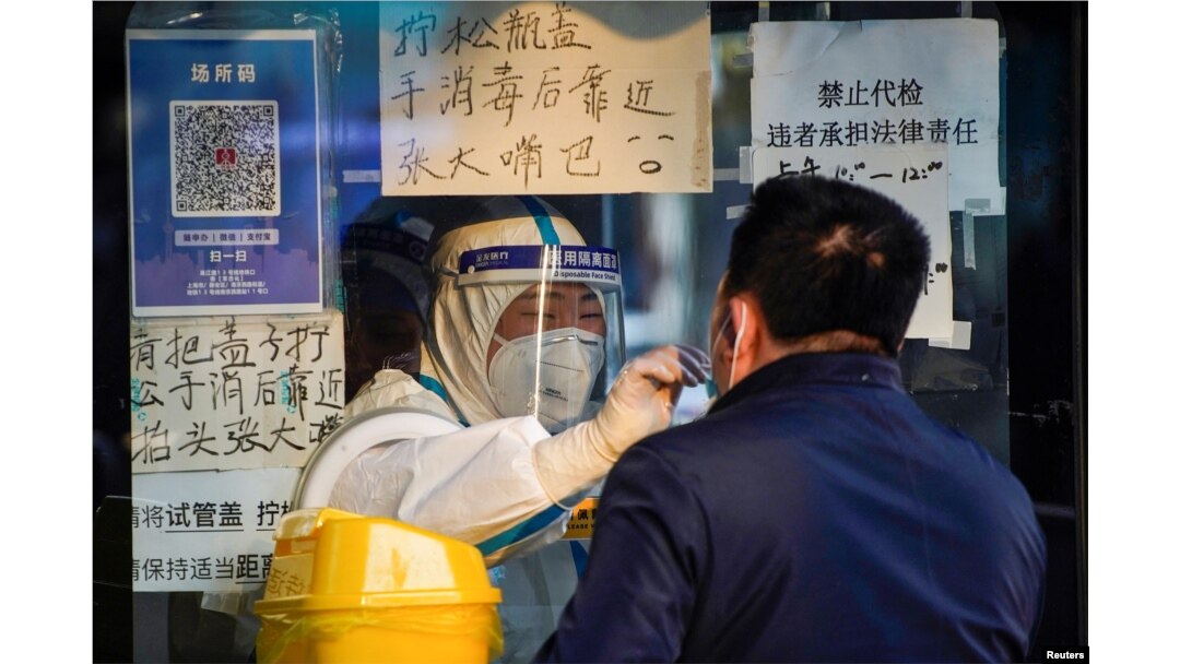 Seorang nakes mengenakan APD mengumpulkan sampel swab dari seorang pria di tempat pengujian asam nukleat, saat wabah virus COVID-19 terus berlanjut di Shanghai, China, 12 Desember 2022. (REUTERS/Aly Song)