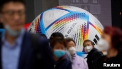 戴著口罩的上海民眾走過2022卡塔爾世界杯比賽用球模型。 （2022年11月23日）