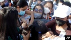 NagaWorld casino workers hold hands to protect security personal during a rally in Phnom Penh on January 4, 2022. Labor union leader Chhim Sithar was arrested for the first time that day en route to take part in the strike. (Heng Sinith/AP)