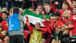 Tim Maroko berfoto bersama di lapangan, memegang bendera Palestina, setelah memenangkan pertandingan sepak bola babak 16 besar Piala Dunia antara Maroko dan Spanyol, di Education City Stadium di Al Rayyan, Qatar, Selasa, 6 Desember 2022. ( Foto: AP/Martin Meissner)