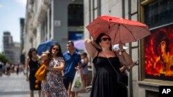FILE - A woman holds an umbrella to shelter from the sun during a hot sunny day in Madrid, Spain, July 18, 2022. 