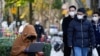 Seorang wanita yang mengenakan masker melihat laptopnya di jalan, saat wabah COVID-19 masih terus terjadi di Shanghai, China, 14 Desember 2022. (Foto: Reuters)