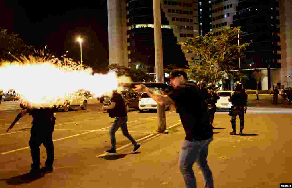 A police officer fires a shotgun as supporters of Brazil&#39;s President Jair Bolsonaro protest after supreme court justice Alexandre de Moraes ordered a temporary arrest warrant of indigenous leader Jose Acacio Serere Xavante for alleged anti-democratic acts, in Brasilia, Dec. 12, 2022.