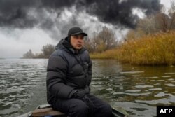Alas isplovljava u svom čamcu na rijeci Dnjepar, dok se crni dim podiže nakon napada na skladište nafte u Hersonu, 20. novembra 2022, tokom ruske invazije na Ukrajinu.