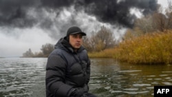 A fisherman sails his boat on the Dnipro River as black smoke rises after an attack on an oil reserve in Kherson, on Nov. 20, 2022, amid the Russian invasion of Ukraine.