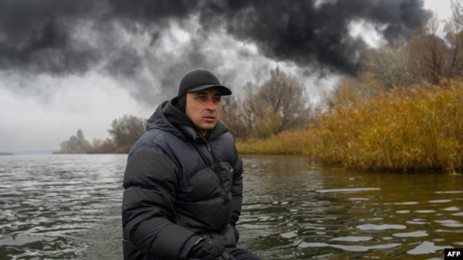 Un pescador navega en su bote por el río Dnipro mientras se eleva humo negro después de un ataque a una reserva de petróleo en Kherson, el 20 de noviembre de 2022, en medio de la invasión rusa de Ucrania.