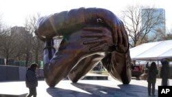 Passers-by walk near the 20-foot-high bronze sculpture "The Embrace," a memorial to Dr. Martin Luther King Jr. and Coretta Scott King, in the Boston Common, Jan. 10, 2023, in Boston. 