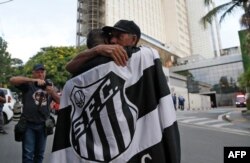 A fan of Brazilian football legend Pele wrapped in a flag of Brazilian team Santos embraces another fan outside the Albert Einstein Israelite Hospital, where Pele died after a long battle with cancer, in Sao Paulo, Brazil, Dec. 29, 2022.