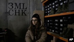 Co-founder Kseniia Drahaniuk of the nonprofit group Zemliachky pauses during an interview in front of shelves stacked with military boots at its supply room in Kyiv, Ukraine, on Tuesday, Dec. 6, 2022. (AP Photo/Vasilisa Stepanenko)
