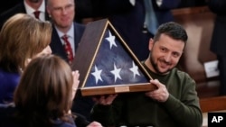 El presidente de Ucrania, Volodymyr Zelenskyy, sostiene una bandera estadounidense regalada por la entonces líder de la Cámara de Representantes de EEUU, Nancy Pelosi, junto a la vicepresidenta Kamala Harris, en el Capitolio, Washington, el 21 de diciembre de 2023.