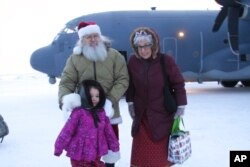 Santa and Mrs. Claus pose with a child who braved winds chills of about minus 25 degrees to greet them when they landed in Nuiqust, Alaska, Nov. 29, 2022.