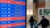 Los viajeros caminan mientras un panel de video muestra retrasos y cancelaciones de vuelos en el Aeropuerto Nacional Ronald Reagan de Washington en Arlington, Virginia, el miércoles 11 de enero de 2023. (Foto AP/Patrick Semansky)