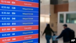 Los viajeros caminan mientras un panel de video muestra retrasos y cancelaciones de vuelos en el Aeropuerto Nacional Ronald Reagan de Washington en Arlington, Virginia, el miércoles 11 de enero de 2023. (Foto AP/Patrick Semansky)