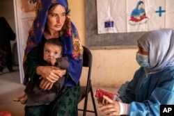 FILE - A Save the Children nutrition counselor, right, explains to Nelab how to feed her 11-month-old daughter, Parsto, with special food, in Sar-e-Pul province of Afghanistan, Thursday, Sept. 29, 2022. (Save the Children via AP, File)