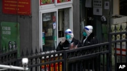 Workers in protective suits buy their breakfast from a store in a locked-down neighborhood as part of COVID-19 controls in Beijing, Nov. 24, 2022. China is expanding lockdowns as its number of COVID-19 cases hit another daily record.