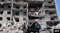 FILE - A war crimes prosecutor, center, looks at a destroyed building with workers after the building was hit by a missile strike in the Ukrainian town of Sergiyvka, near Odesa, killing at least 18 people and injuring 30, on July 1, 2022.